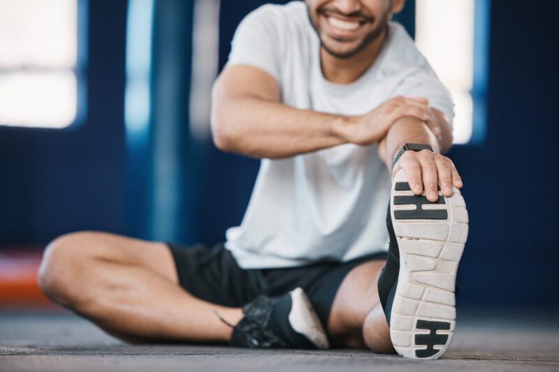 Foot, exercise and stretching with a sports man in the gym getting ready for a cardio training routine. Fitness, health and warm up with a male athlete in preparation of a workout for wellness