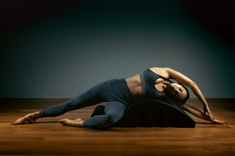 Pilates, fitness, sport, training and people concept woman doing exercises on a small barrel. Fitness concept, low key, gray background, copy space, art light.