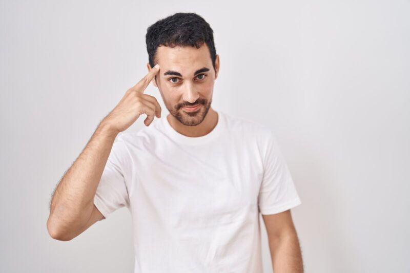 Handsome hispanic man standing over white background smiling pointing to head with one finger, great idea or thought, good memory