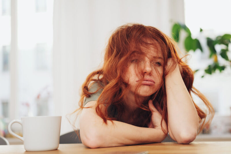 Red haired girl sitting at table with boring face