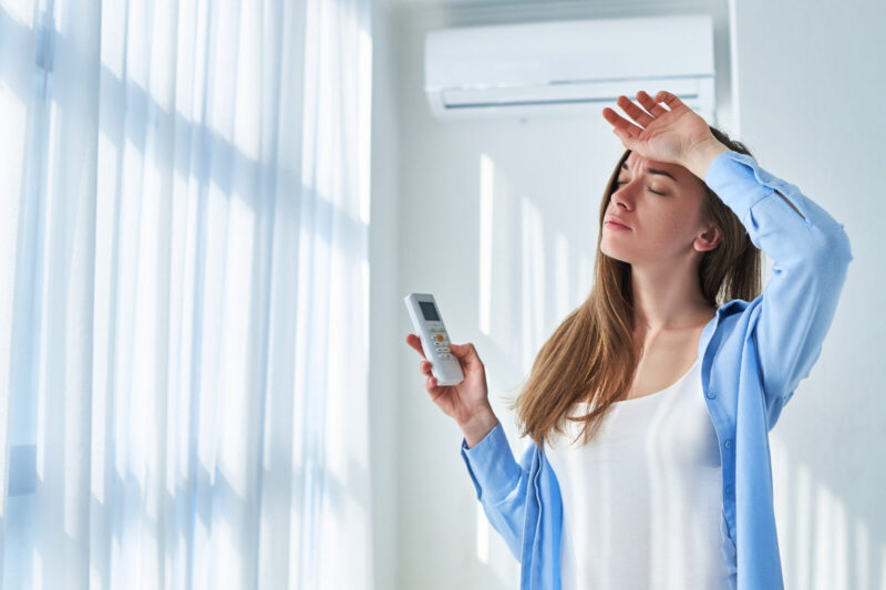 Sweating woman suffering from heat and hot weather cools down with air conditioning at home. Refresh concept