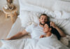 Young caucasian sleeping couple in bed. Handsome beardy European man laying with wife at bedroom enjoying Sunday morning. Calm hispanic young adult woman having nap at hotel with husband.